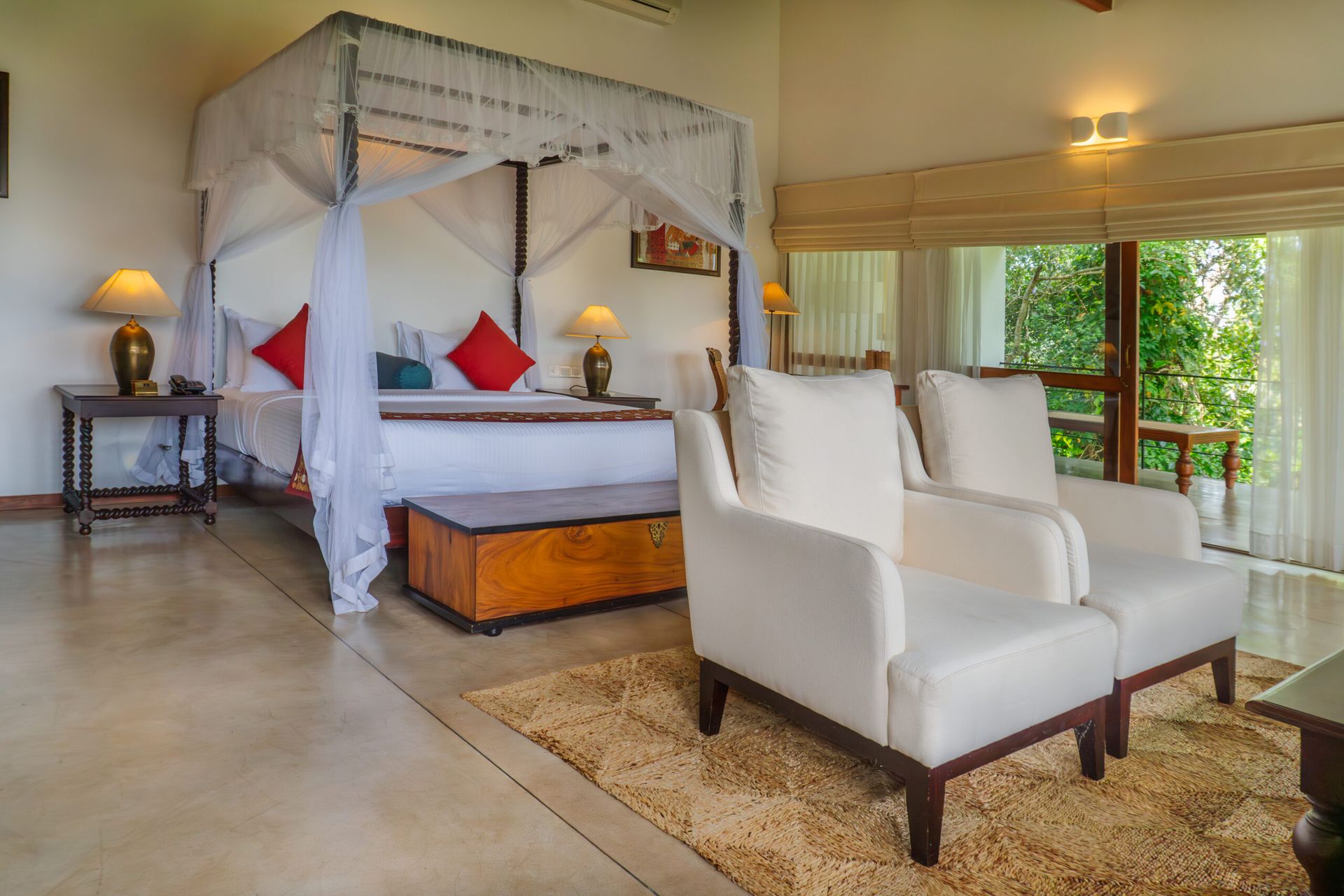 A suite with a netted canopy bed, 2 white armchairs and windows onto trees
